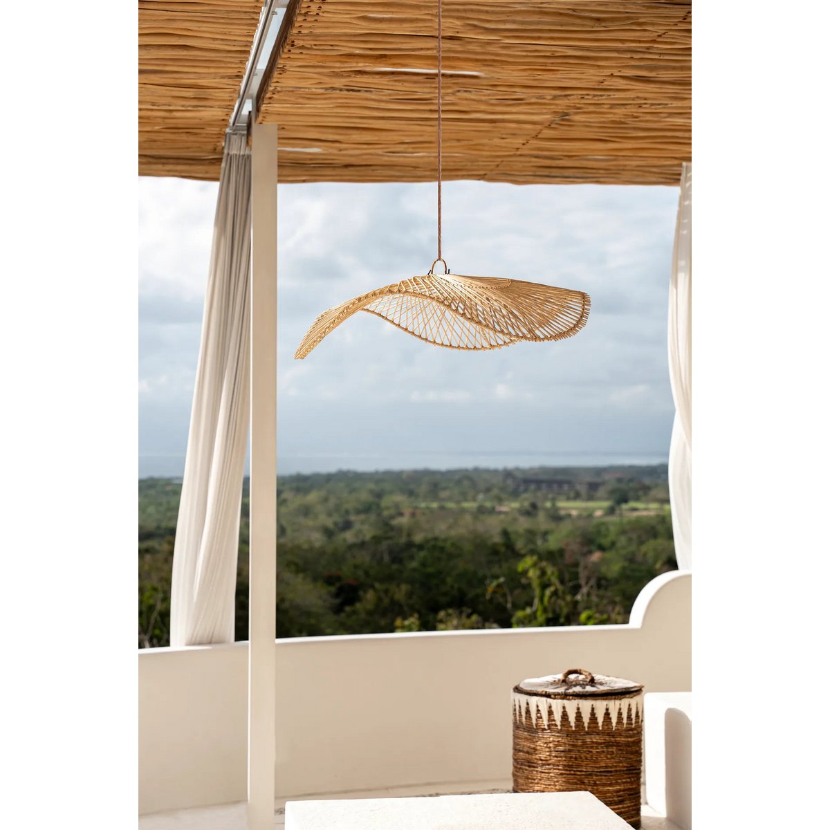 Loom Rotan Hanglamp in een buitenruimte, biedt subtiele verlichting en stijl boven een loungebank onder een overkapping.