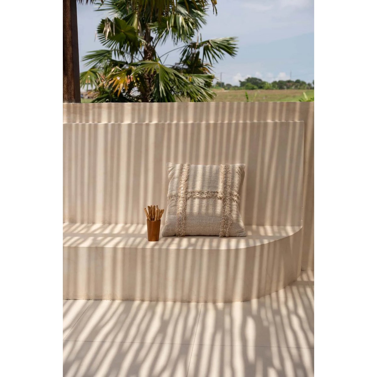 Beige boho kussenhoes buiten in de zon op betonnen bank