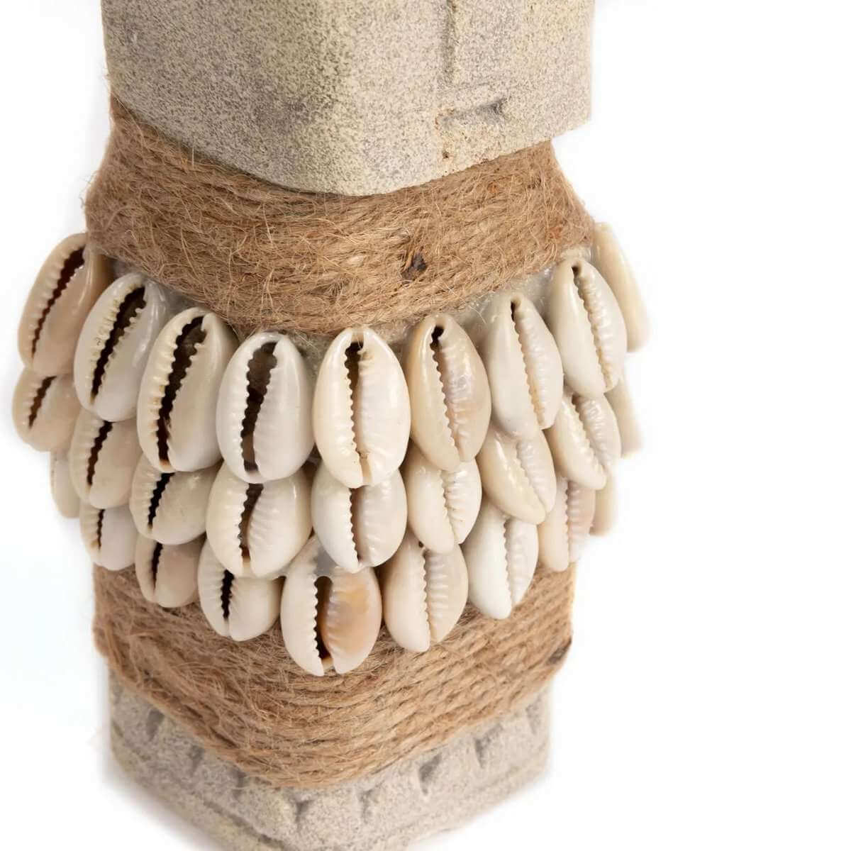 Close-up van schelpen en touw rondom het zandstenen Sumba beeldje, traditioneel handgemaakt