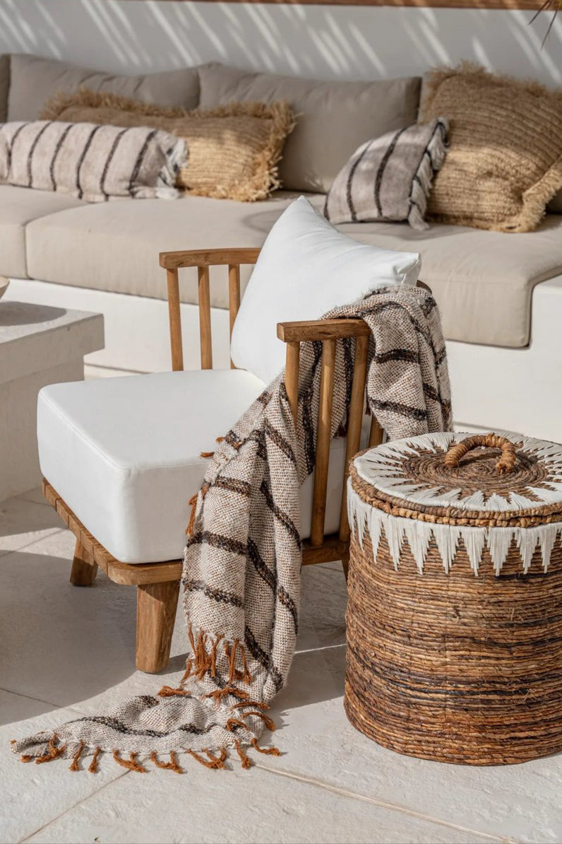 Boho terrasdecoratie met Ibiza Stripe kussens, houten stoel met wit kussen, een warm plaid en een rotan opbergmand.