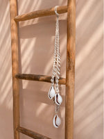 detail van handgemaakte kauri schelpenketting op houten ladder