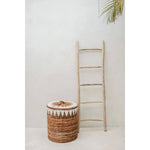 Boho mand in natuurlijk interieur naast houten ladder en wit gestucte muur