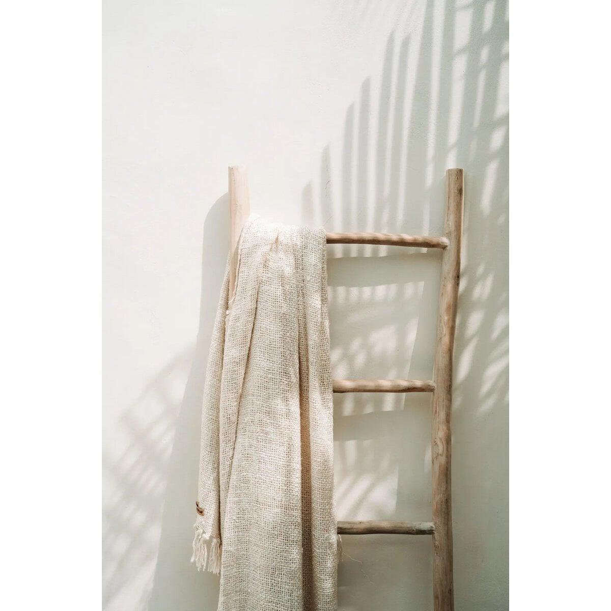 Beige Safi Deken op ladder tegen witte muur, minimalistische styling.