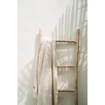 Beige Safi Deken op ladder tegen witte muur, minimalistische styling.