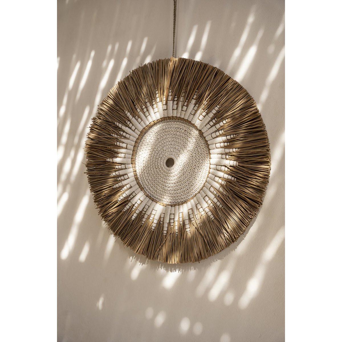 Ronde Soluna wanddecoratie van raffia en wit macramé aan een lichte muur in bohemian sfeer