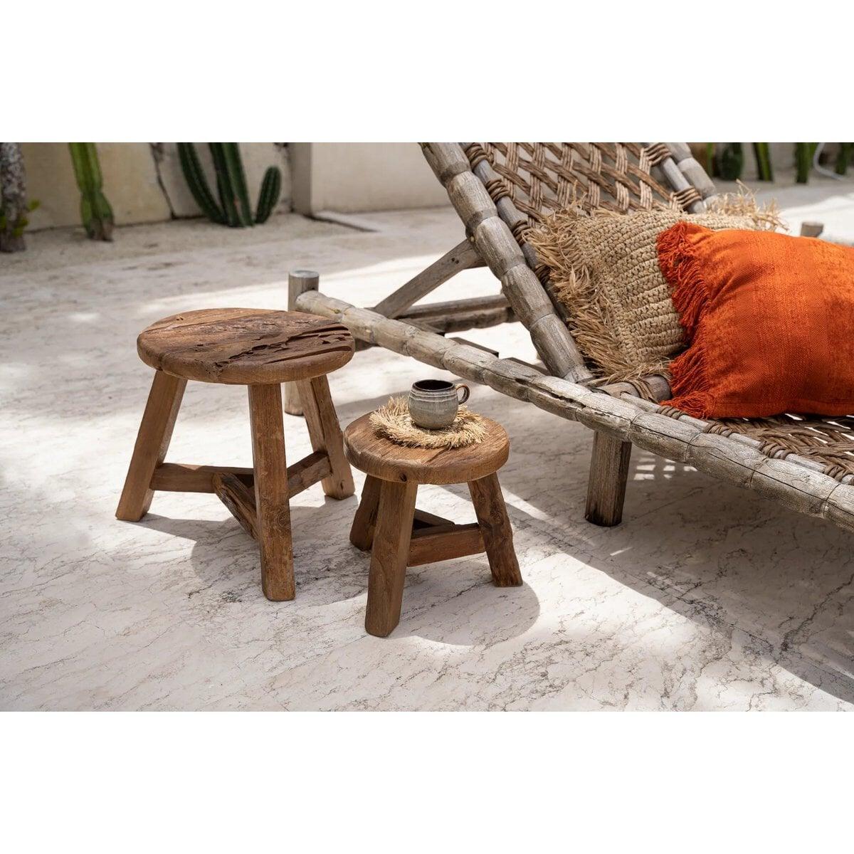 Set van twee teakhouten krukken in zonnige bohemian buitenruimte met rotan loungebank